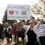 People in Denver protesting the federal government's stance on immigration; one holds a white posterboard that reads "Aurora loves immigrants"