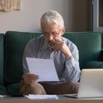 A senior man sitting on a couch intensely analyzing an expense bill.