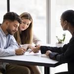 A realtor guiding a couple on signing a property contract.