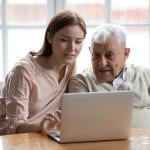 A senior man with his caregiver browsing the internet using a laptop.