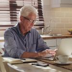 A senior man using a laptop in his kitchen.