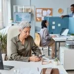 A senior businesswoman working at her desk in an open office setting.