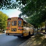A yellow school bus waits by a bus stop in a family neighborhood in Fairfax County, Virginia.