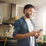 A man his apartment's kitchen looking up renovation ideas in his phone.