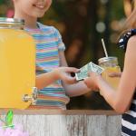 A young girl sells lemonade to another young girl at the park.