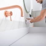 A handyman installs copper faucet to a modern marble wall bathroom.