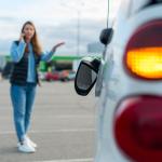 Woman talking on her phone while looking at her car's broken left side rear-view mirror.