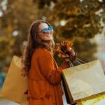 A happy stylish woman holding shopping bags and autumn leaves.