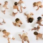 A group of diverse babies crawling on a white floor.