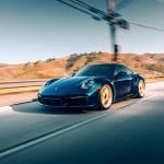 A black Porsche Turbo S driving on a highway with mountains in the background.