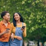 Two women having coffee while walking in a park.