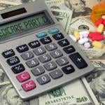 Medicare Part D text on a calculator with prescription pills spilling from bottle on top of US banknotes.