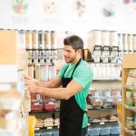 A zero-waste grocery store owner arranging stock of items on shelves.