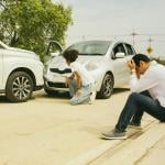 Drivers of two cars caught in a road accident inspect and sit down by a roadside in distress.