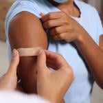 A doctor puts adhesive bandage on a woman's arm after vaccination.