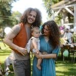 A happy couple pose with their baby at a backyard party.