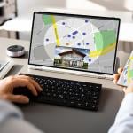 Person looking up a map view of a property's location using a laptop and a phone.