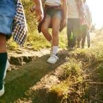 Close up of young campers' legs as they hike downhill in a forest path.