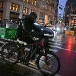A rider transports a delivery using an e-bike on a street in midtown Manhattan on a rainy night on December 22, 2024 in New York City, USA. 