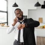 A black businessman on the phone looks at his wrist watch as he gets ready to go to work in the morning.