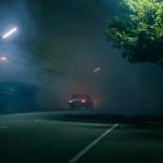 A classic car drives down a spooky road at night.