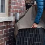 A woman covers their air conditioning unit set outside the house.