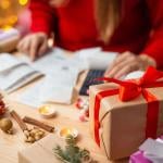 A woman calculates expenses on a table with holiday gifts and decorations.