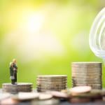 A miniature elderly couple stands on a stack of coins leading to a glass jar full of savings.