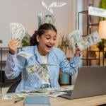Young person throwing money and bills in the air in front of a computer; concept of getting rich quickly myth
