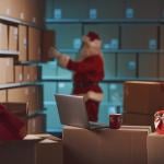 A worker dressed as Santa Claus prepares delivery Christmas gift boxes in a warehouse.