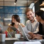 Five members of a business team talking together at a table with laptops open. 