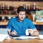 A male restaurant owner calculating business bills.