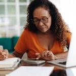An elderly black woman calculating finances at home.