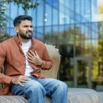 A young man nervously sitting on a bench outdoors experiencing chest pains.
