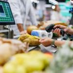 A supermarket cashier staff scans a bag of potatoes at a checkout counter.