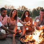 A group of four friends around a campfire grilling s'mores.