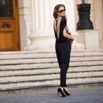 A stylish, tall woman wearing a black, backless suit poses for a street fashion photograph.