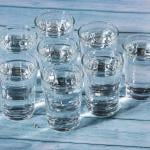 Eight glasses of water on a wooden table.