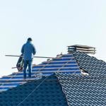 Workers installing metal tile on the roof while roofing house in construction site.