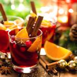 Christmas mulled red wine with spices and oranges on a wooden rustic table with evergreen decor and pine cones in the background.