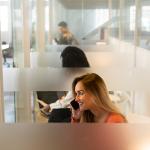 A woman at an office's phone booth taking a call with her smartphone.
