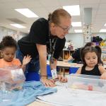 Head Start teacher Sasha Fair helps two preschool children with a science experiment.