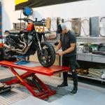 Unrecognizable mechanic man checking engine of custom motorcycle over platform.