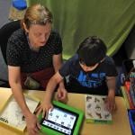 An instructional assistant helping an autistic student with a lesson or activity from a tablet.