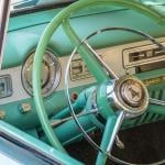 A close up view on a vintage pastel green car's steering wheel.