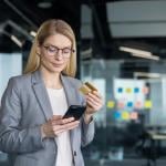 A businesswoman holding a phone and a credit card in an office.
