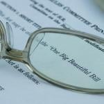 A pair of eyeglasses magnified on the words 'One Big Beautiful Bill' (Act) on a document.