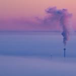 Smoke coming out of a heat and power plant chimney, blending with a lavender morning sky.