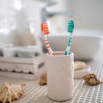 Two colorful toothbrushes in a ceramic glass against the background of a bathroom's washbasin.