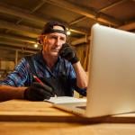 A senior male carpenter working with a client online from their workshop.